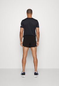 Svarta träningsshorts och en mörk t-shirt med korta ärmar och en logotyp på vänster ärm, kombinerat med sneakers.