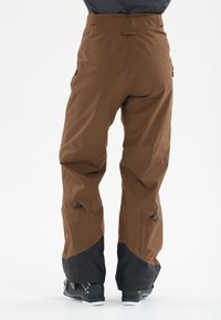 Braune wasserdichte Skihosen mit tailliertem Design, schwarzen Unterschenkeln, seitlichen Reißverschlüssen und verstellbaren Bündchen für verbesserte Passform und Schutz.