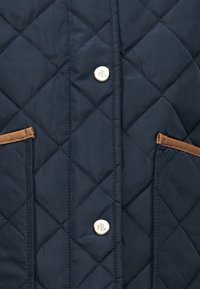 Μπλε ναυτικό μπουφάν με ρόμβους, καφέ τσέπες με λεπτομέριες και ασημένια λογότυπα. Λείο ύφασμα με απαλό άγγιγμα.