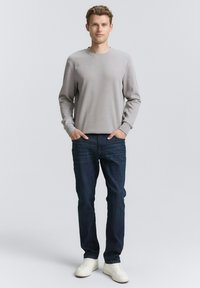 Lichtgrijze longsleeve met geribde manchetten, gecombineerd met donkerblauwe jeans en witte sneakers. Eenvoudig ontwerp; geen zichtbare patronen of grafische elementen.