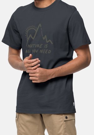 Mann trägt dunkelgraues T-Shirt mit Berg- und Sonnenmotiv sowie dem Text „Nature is all you need“, kombiniert mit beigen Cargo-Shorts.