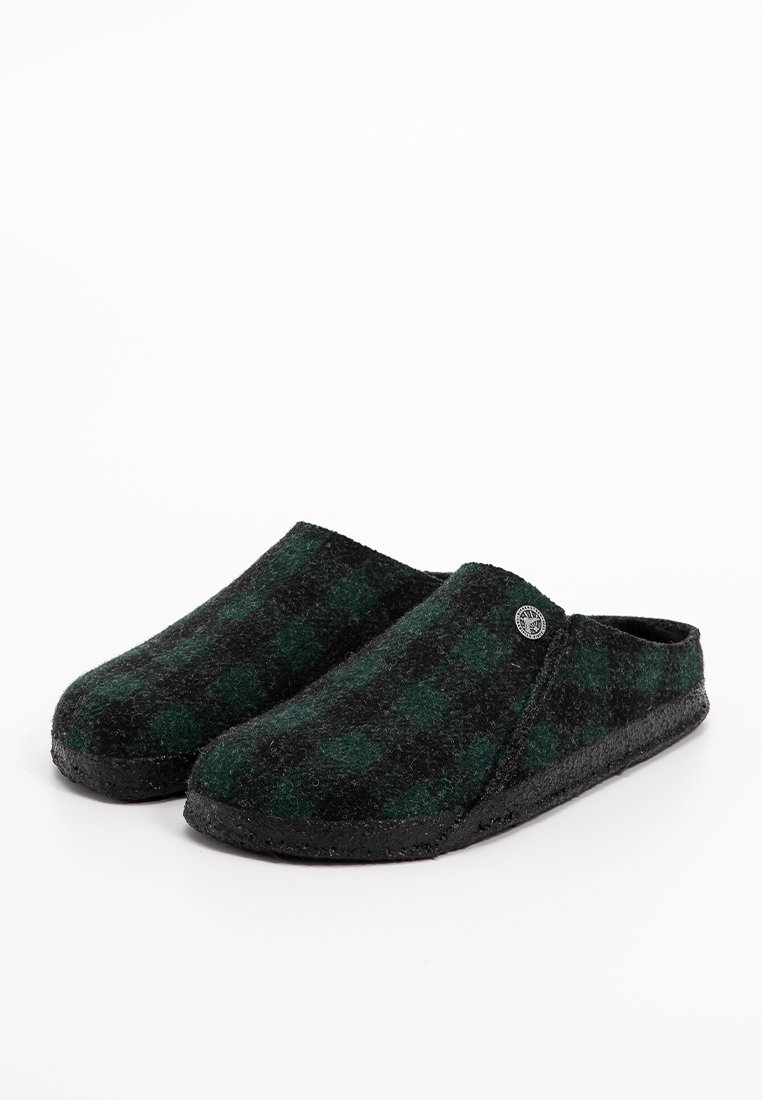 Ein Paar schwarze und dunkelgrüne Karoschlafsacken aus einem Slip-On-Design mit einem runden metallischen Logo an der Seite und strukturierten schwarzen Sohlen.