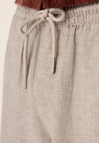 Pantalons beige clair à cordon de serrage fabriqués dans un tissu texturé et tissé. Présentent une coupe décontractée, une taille élastique et des cordons de serrage avec embouts métalliques.