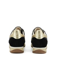 Un paio di sneakers nere e oro con il logo "70" sul tallone e il testo "BACK 70" sulla suola, viste da dietro su uno sfondo bianco.