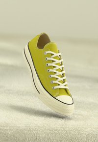 Adidași din pânză verde lime cu șireturi albe, vârf din cauciuc și bandă contrastantă neagră la talpă, având un design cu profil jos.