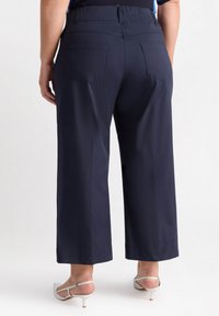 Granatowe spodnie szerokie w nogawkach z wysokim elastycznym pasem i dwoma tylnymi kieszeniami. Materiał wydaje się gładki, z prostym krojem ku dołowi.