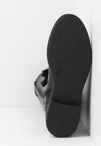 Chaussure noire avec une semelle en caoutchouc texturée, présentant des détails sur la tige, avec un bout renforcé et des accents latéraux.