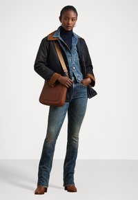A brown leather shoulder bag, black jacket with tan collar, layered denim jacket, dark blue jeans, and brown heeled ankle boots.