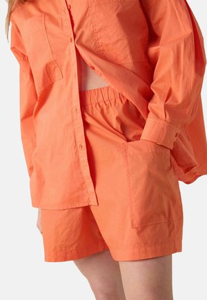 Chemise en coton orange avec deux poches, coupe oversized ; short orange assorti avec ceinture élastique et détails de poches latérales.