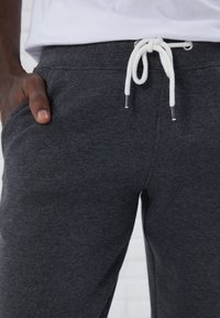 Pantalones de chándal gris oscuro con cinturilla, cordón blanco y bolsillos laterales, con una textura de toalla suave y un diseño casual.