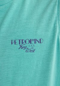 Turkise t-shirt lavet af blødt stof med et lilla trykt logo, der siger "PETROLIND U.S.A Key West" centreret på fronten.