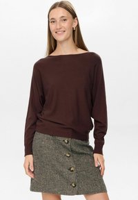 Brauner, locker sitzender Pullover mit schulterfreier Ausschnitt, kombiniert mit einem rock im Fischgrätenmuster mit goldenen Knöpfen.