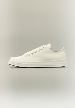 Pantof sport alb din pânză, cu talpă de cauciuc albă, protecție pentru vârf și șireturi albe, prezentat din profil pe un fundal neutru.