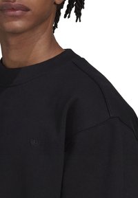 Svart sweatshirt med ribbad halsringning och axelsömmar. Har en liten, broderad svart logotyp på framsidan. Mjuk tygkänsla.