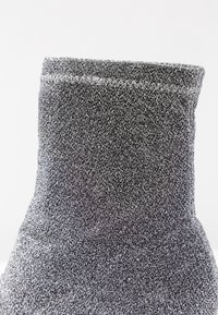 Chaussette thermique grise avec un tissu épais et texturé. Elle présente un bord côtelé et des coutures en zigzag sur le bord supérieur. Design doux et chaud.