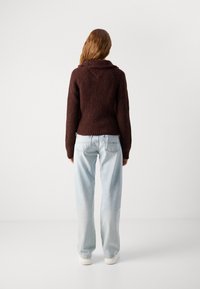 Bordeaux gebreide trui met een colsjaal en een textuurpatroon, gecombineerd met lichtblauwe wijde jeans. Zichtbare stiksels en ribbeldetails.