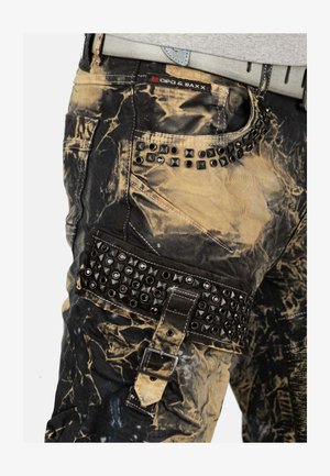 Cipo & Baxx cargo pants featuring a black and gold distressed design, studded accents, a buckle strap, and multiple pockets.
