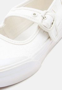 Λευκό αθλητικό παπούτσι Mary Jane με γκλίτερ φινίρισμα, ρυθμιζόμενο λουρί με αγκράφα και παχιά ελαστική σόλα, με εσωτερικό από υφασμάτινο καμβά με υφή.