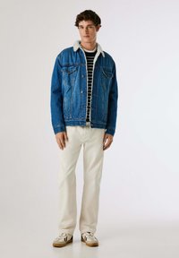 Blå denimjacka med en mjuk vit krage, i kombination med en svart och vit randig skjorta samt krämfärgade byxor. Bärs med avslappnade sneakers.