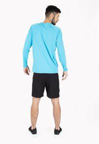 Langærmet turkis sportstrøje parret med sorte shorts. Trøjen har et forenklet design med en glat overflade og tætsiddende stil.