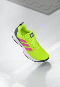 Neon gul atletik sko med pink striber, mesh overdel, polstret krave og kontrasterende grå hæl. Gummisål for godt greb.