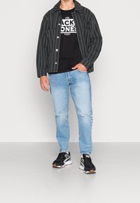 Černá a šedá pruhovaná košile, černé tričko s potiskem, světle modré džíny a černé tenisky se šedými a bílými detaily.