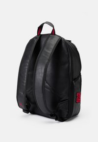 Mochila de couro preta com alças duplas, compartimentos com fecho e detalhe bordado em vermelho "23". Textura suave com design minimalista.