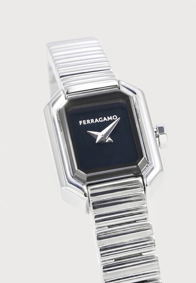 Ασημένιο ρολόι Ferragamo με ορθογώνιο μαύρο καντράν και μινιμαλιστικούς δείκτες ώρας και λεπτών, προσδεδεμένο σε μεταλλικό μπρασελέ.