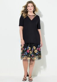Top negro con escote en V y mangas cortas, combinado con una falda negra con bordados florales coloridos y una superposición de tul. Tacones negros.