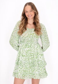Rochie florală verde cu mâneci lungi, având o talie elastică și volane stratificate. Construită dintr-un material ușor, cu modele de flori albe pe toată suprafața.