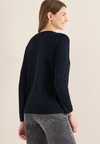 Granatowa koszulka z długim rękawem wykonana z miękkiej tkaniny, z okrągłym dekoltem i luźnym krojem, zestawiona z teksturowanymi szarymi dżinsami.