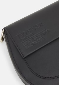 Mustan nahkainen clutch-laukku, jossa on kohokuvioitu brändilogo, pyöreä muoto, magneettisuljenta ja hopeanväriset varusteet.