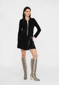 Fekete cipzáras dzseki nagy gallérral, fekete miniszoknyával párosítva, amely oldalán cipzárral és lapos fémrátétekkel díszített. A megjelenést térdig érő kígyómintás csizmák teszik teljessé.