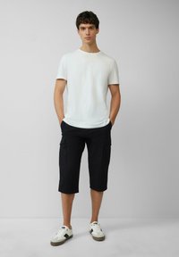 Witte short-sleeve t-shirt gecombineerd met donkere cargoshorts, voorzien van zijzakken en tot de knie snit. Draag het met witte en grijze sneakers.