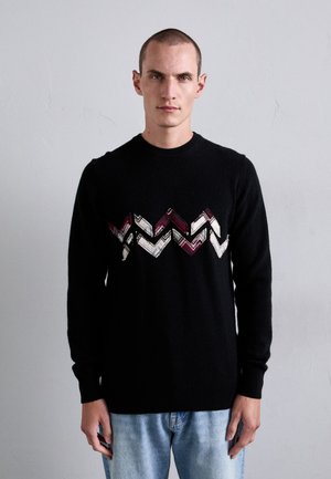 Schwarzer gestrickter Pullover mit einem Zickzackmuster in Rot, Weiß und Creme über der Brust. Klassischer Rundhalsausschnitt und gerippte Bündchen.