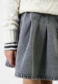 Grijze geplooide denimrok met een gestructureerd oppervlak, gecombineerd met een gebreide crèmekleurige trui met een kabelpatroon en gestreepte manchetten.