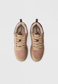 Braune und beige Sneaker mit einer strukturierten Oberfläche, Mesh-Details und rundem Zehenbereich. Sie verfügen über flache Schnürsenkel und eine Lasche an der Ferse.