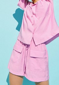 Camisa de botones de manga corta rosa y pantalones cortos a juego, hechos de tela ligera, con un corte holgado y bolsillos frontales.