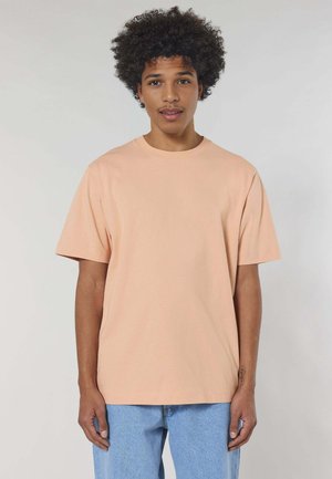 Licht perzik kleurige katoenen t-shirt met een ronde halslijn en korte mouwen, met een ontspannen pasvorm. Gecombineerd met licht blauwe jeans.