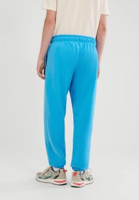 Zili sporta bikses ar elastīgu jostu un sānu kabatām, izgatavotas no gludas auduma. Apvienotas ar bēšiem un daudzkrāsainiem kedām.