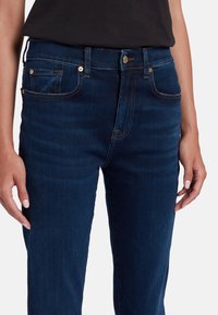 Jeans in denim blu scuro caratterizzati da un design attillato, dettagli classici delle tasche e hardware in tonalità dorata sui bottoni e sui rivetti.