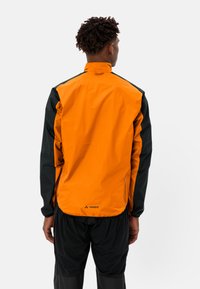 Giacca impermeabile arancione e nera con maniche lunghe, colletto alto e tasche laterali con zip. Presenta un logo nella parte bassa della schiena.