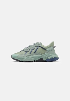 Baskets de sport vert clair et bleu avec semelle texturée et panneaux superposés vues de côté sur un fond uni.