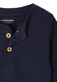 Marineblaue Babykleidung mit zwei beigen Knöpfen, Rundhalsausschnitt und Etikett mit der Aufschrift "vertbaudet 6 mois - 67 cm."