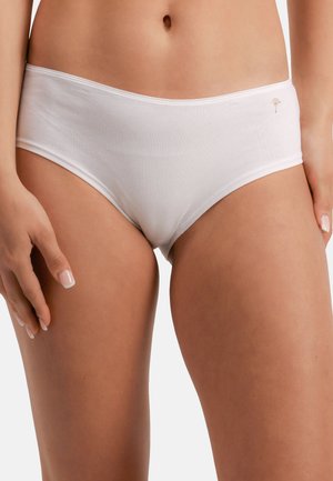 Valkoiset puuvillaiset hipsterialushousut, joita malli käyttää, näkyy vartalo vyötäröstä reisiin asti, kädet rentoina sivuilla.