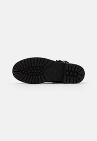 Semelle de chaussure noire avec des rainures profondes pour l'adhérence, en matériau en caoutchouc texturé, et un design arrondi avec des motifs d'étoiles.
