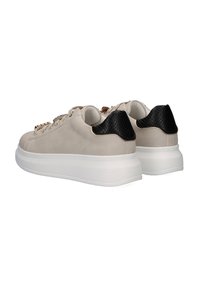 Las zapatillas presentan una parte superior de cuero beige, un talón negro texturizado y una suela gruesa blanca; incluyen detalles en dorado en los cordones.
