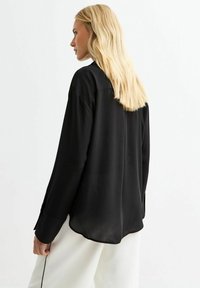Zwarte lange mouwen shirt met een relaxte pasvorm, gladde textuur en ronde zoom. Beschikt over knoopmanchetten en een eenvoudig kraagontwerp.