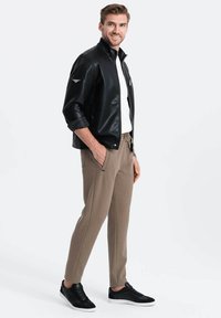 Zwarte leren bomberjack, witte T-shirt met ronde hals, lichtbruine tapered broek en zwarte sneakers. Het jack heeft een rits en zijzakken.