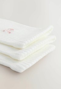Biele rebrované bavlnené ponožky poskladané, s jemným ručne vyšívaným detailom v ružovej farbe. Mäkká textúra a hladké, zaoblené okraje.